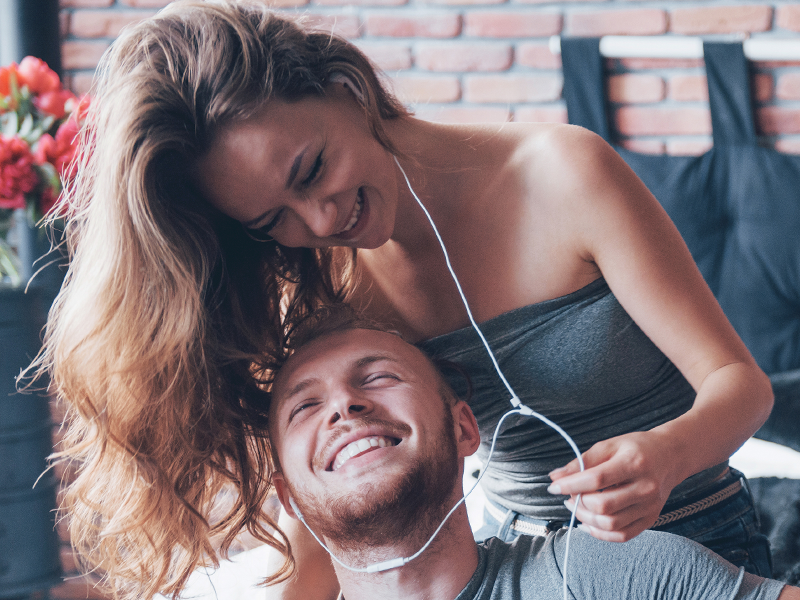 Image of a couple sitting close together sharing a pair of headphones, listening to music and enjoying a relaxed, intimate moment.