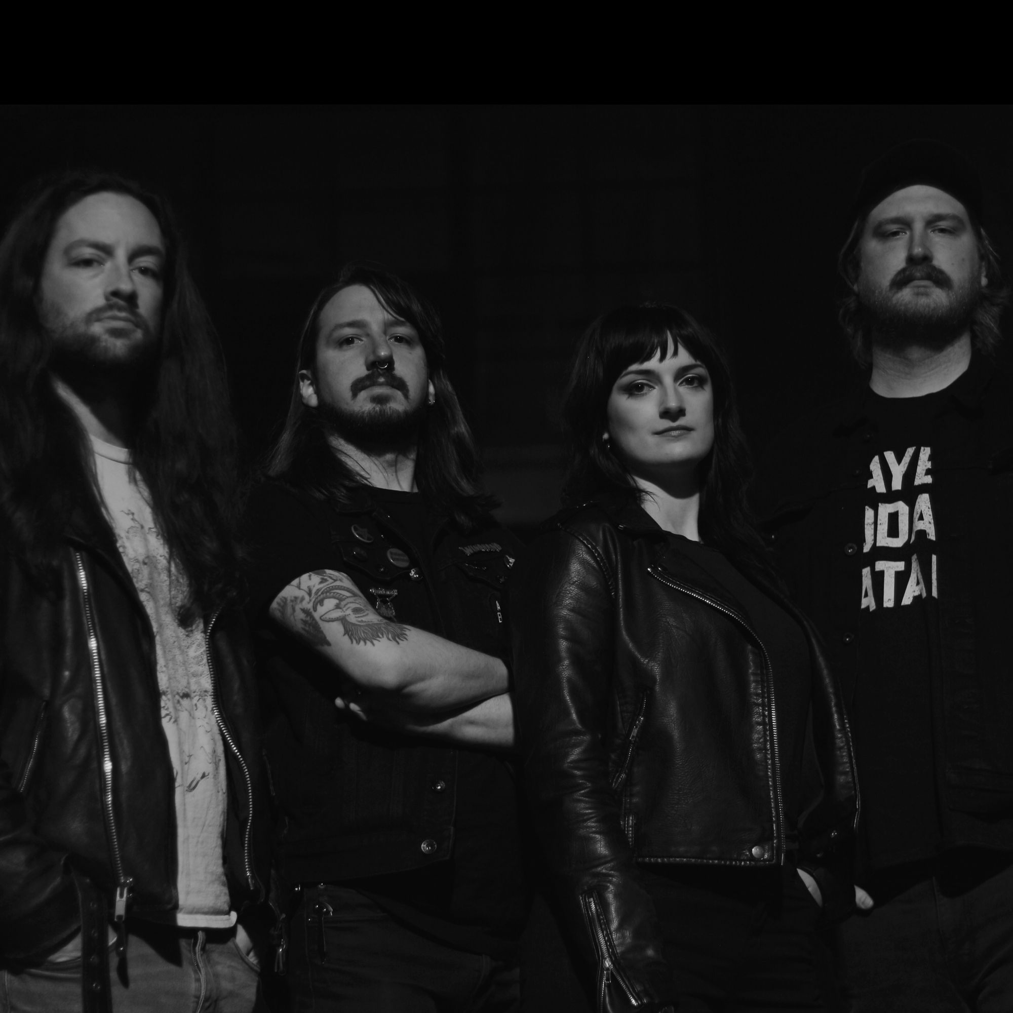 Black and white photo of four band members posing together against a dark background