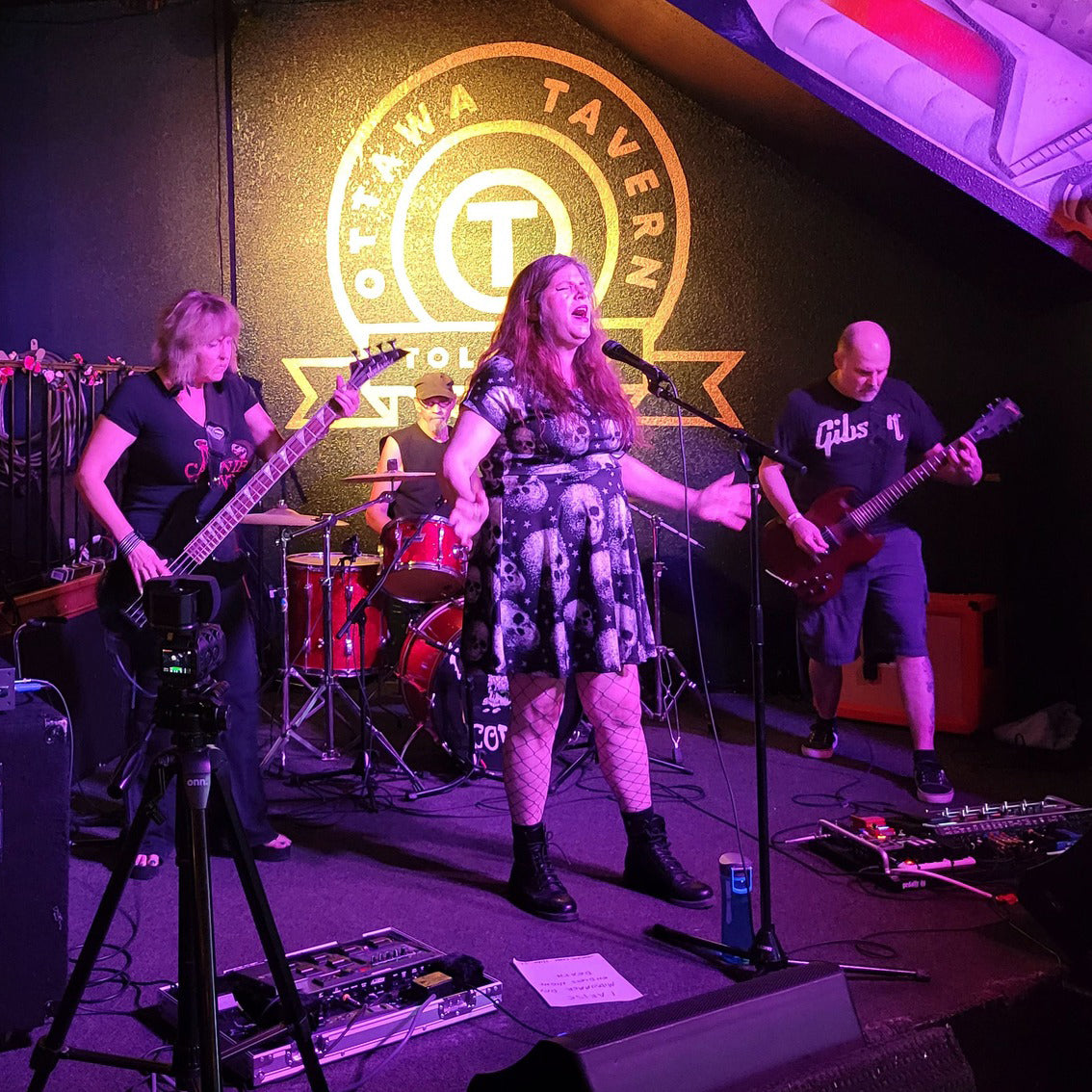 Band performing on stage at the Ottawa Tavern with a prominent logo in the background.